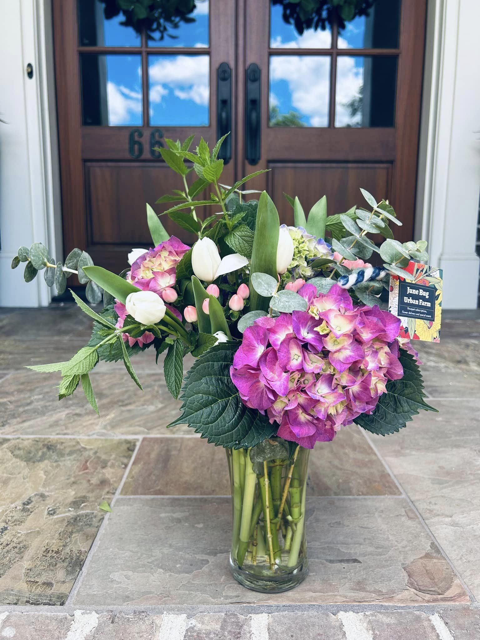 purple hydrangea and assorted flowers in a glass vase sitting on a porch